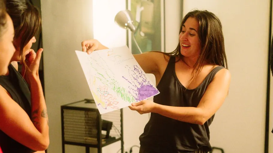 Woman showing colorful drawing to two women indoors.
