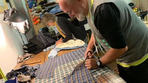 Two tailors cutting plaid fabric on a table.