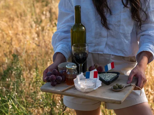 A person is holding a tray of wine and cheese.