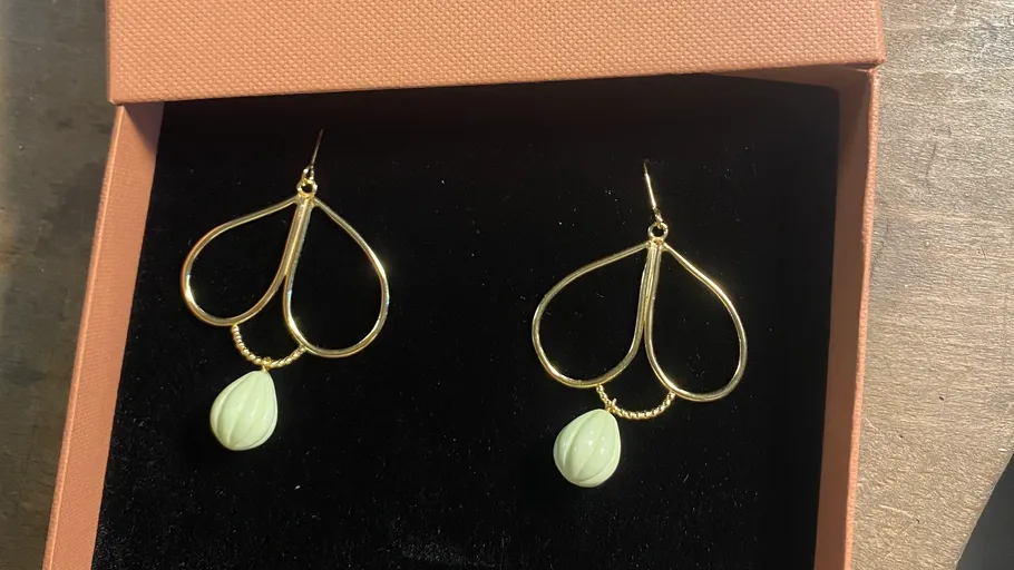 Gold earrings with green gemstones in box.