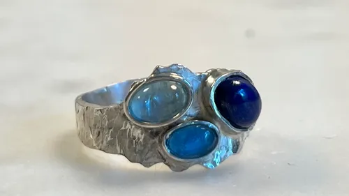 Silberring mit drei blauen Steinen, neutraler Hintergrund.
