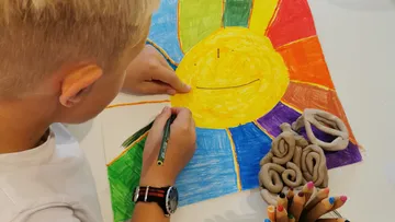 Child drawing colorful sun with crayons.