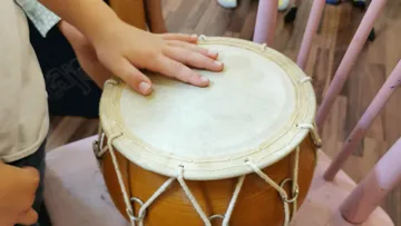 Child's hand playing a drum indoors.