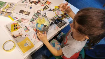 Child crafting with newspapers and glue.