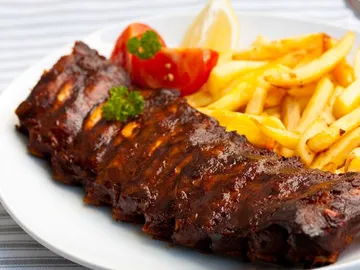 Pork ribs lie on a plate of french fries.
