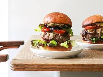 A burger on a plate surrounded by a wooden surface.
