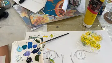 Kunstbedarf auf Tisch mit unfertigem Gemälde.