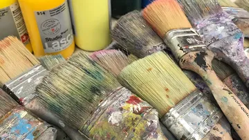 Used paintbrushes beside colorful paint bottles.