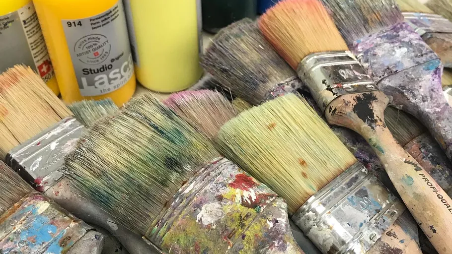 Used paintbrushes beside colorful paint bottles.