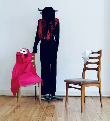 Ankleidepuppe mit Masken und Kleidung zwischen Stühlen.