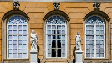 Two statues in front of arched windows.