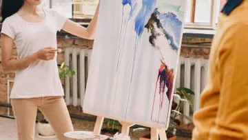 Person painting abstract art on canvas indoors.