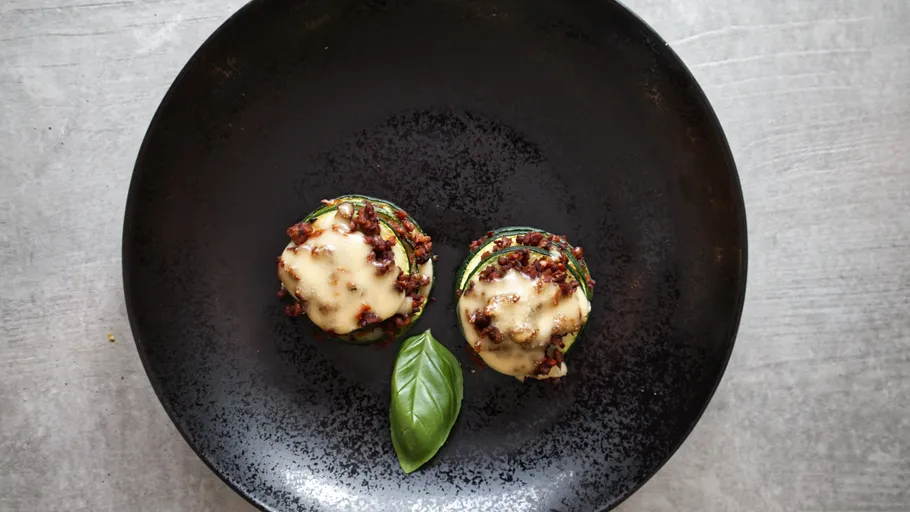 Zwei Zucchini-Türme mit geschmolzenem Käse auf Teller.