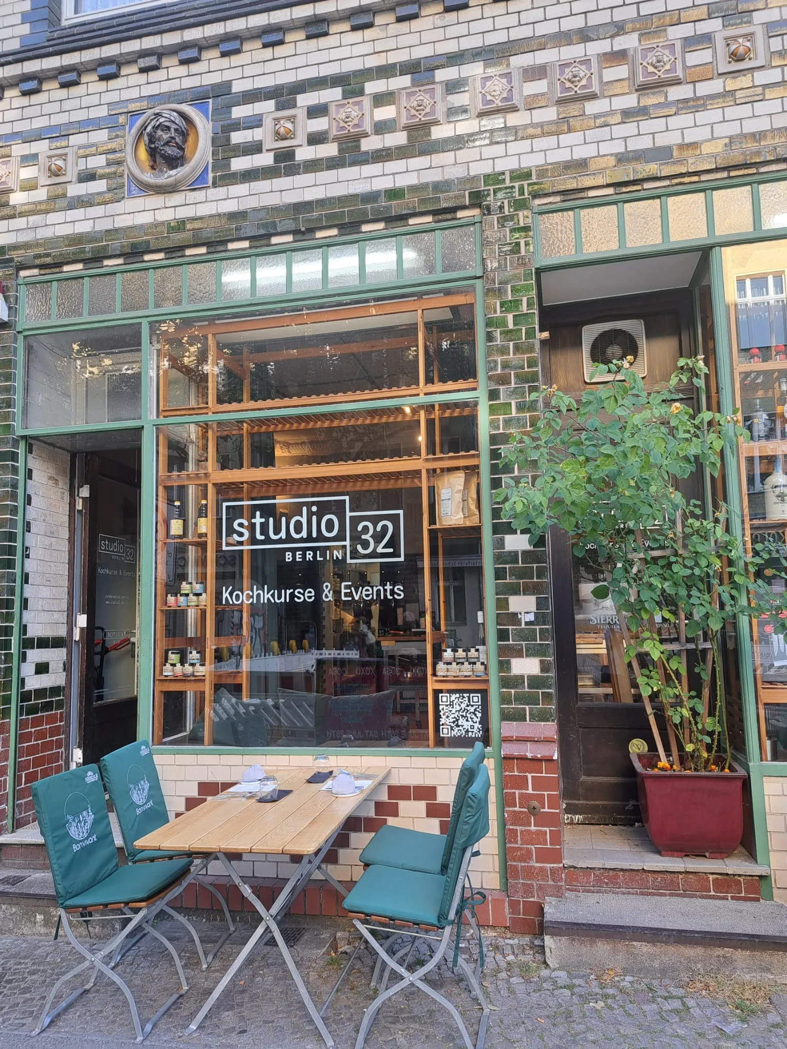 Outdoor table with chairs, in front of colorful storefront.