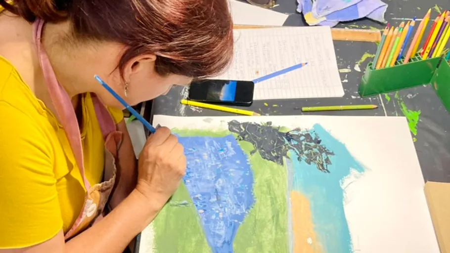 Woman painting landscape on paper indoors.