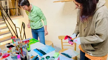 Two women painting at a table with art supplies.