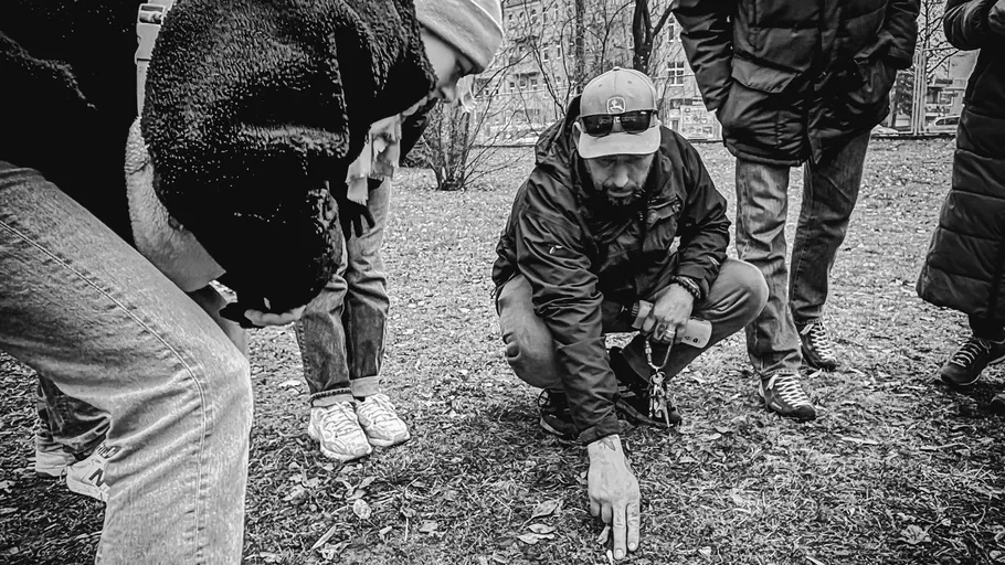 Group observing man pointing at ground outside.
