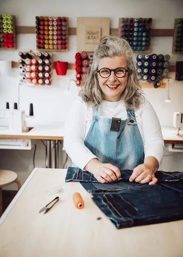 Woman sewing denim, surrounded by colorful threads.