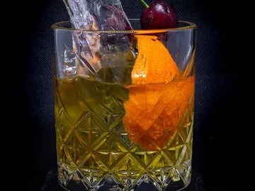 Ein Glas mit Eiswürfeln, Orangenscheibe und Kirsche.