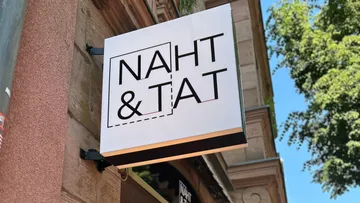 Ladenschild mit 'NAHT & TAT' an Gebäude.