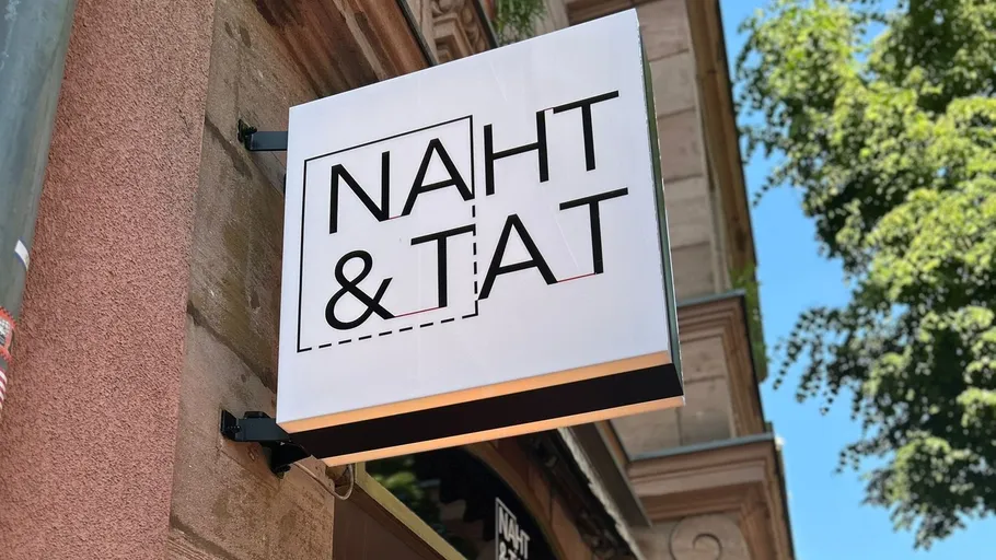 Ladenschild mit 'NAHT & TAT' an Gebäude.