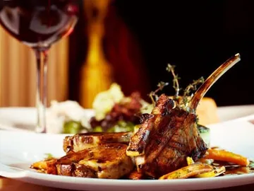 Grilled lamb chop on a plate, with red wine next to it.