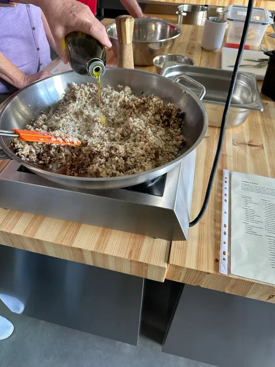 Person adding oil to rice in kitchen.
