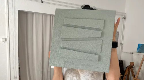 Person holding textured panel in art studio.