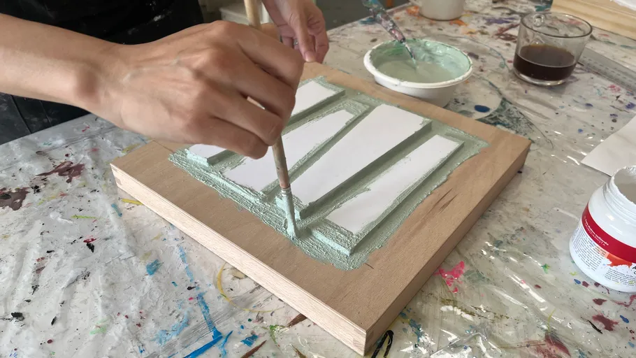 Hands painting green frame on wooden board.