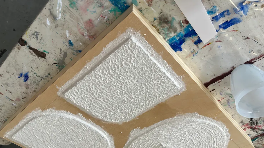 Textured white shapes on wooden board, messy background.