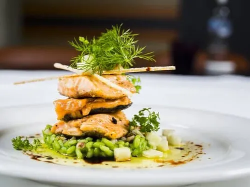 Grilled salmon piled on green risotto, decorated with herbs.