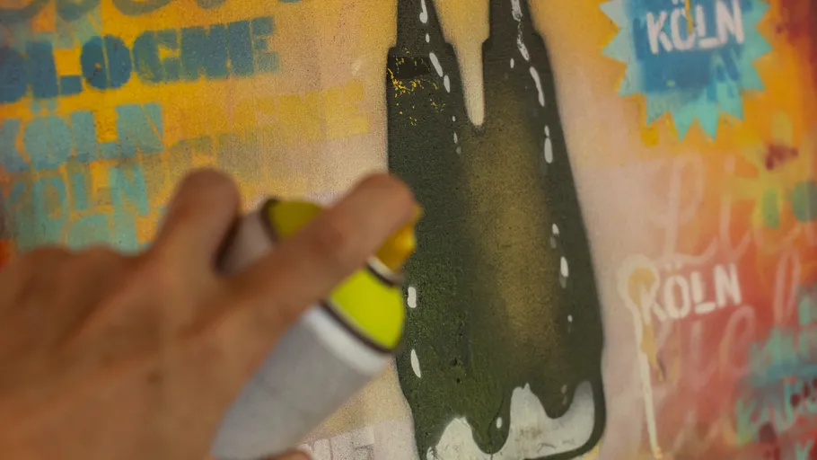 Hand sprays graffiti on colorful wall.