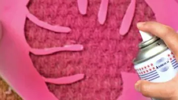 Hand sprüht Schablone auf rosa Oberfläche.