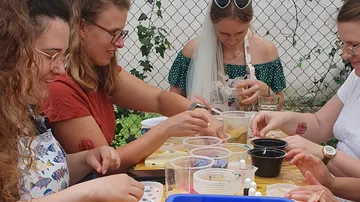 Gruppe bastelt im Freien an Holztisch.