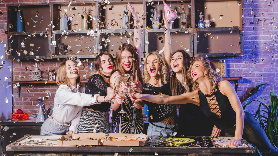 Six women celebrating with confetti indoors.
