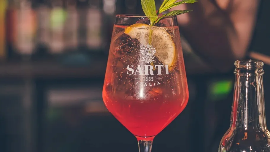 Red cocktail with lemon and mint garnish.