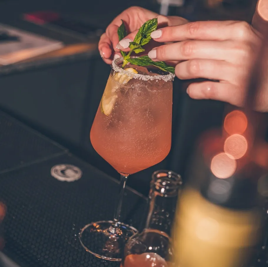 Person garnishing cocktail with mint leaves at bar.