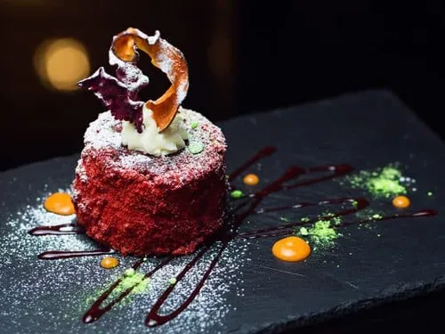Roter Kuchen mit Sahne und dekorativen Saucen auf Platte.