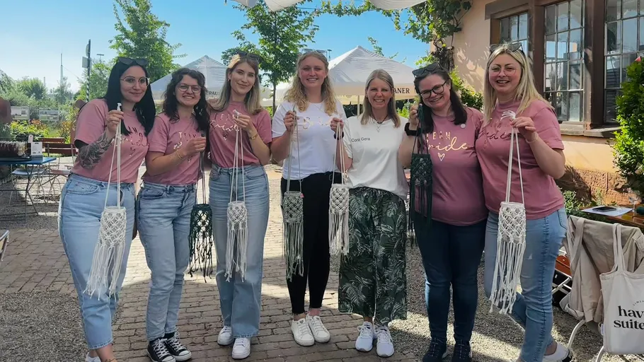 Seven women holding macramé in outdoor setting.