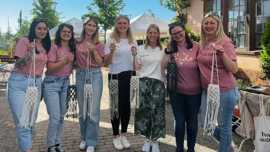 Sieben Frauen halten Makramee-Kunstwerke im Freien.