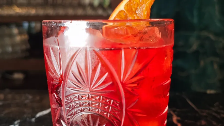 Red cocktail in a decorative glass with orange slice.