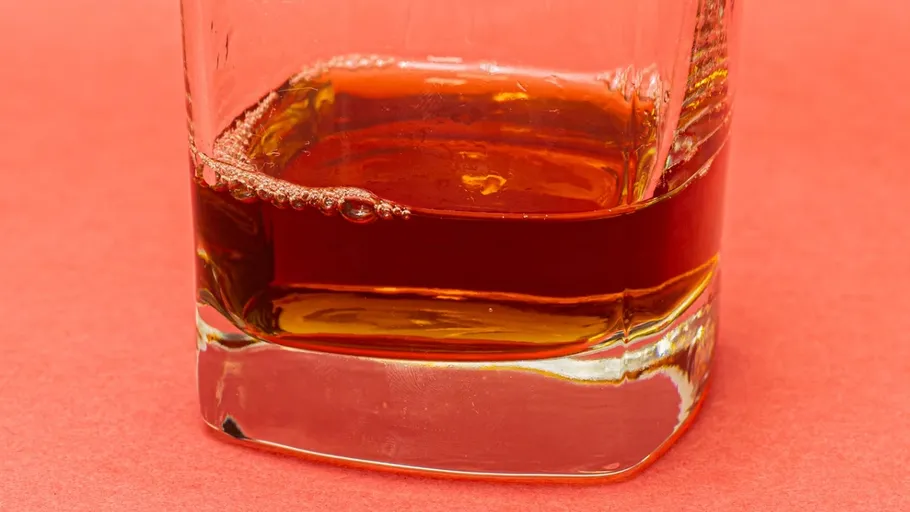 Glas mit Whiskey auf pfirsichfarbenem Hintergrund.