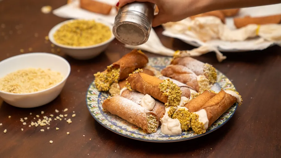 Cannoli being dusted with sugar on table.