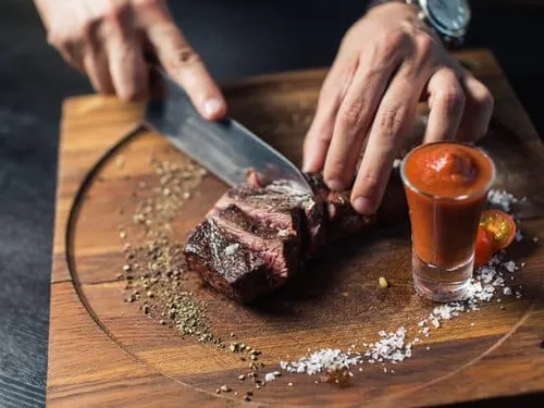 A steak is cut on a wooden board, with sauce.