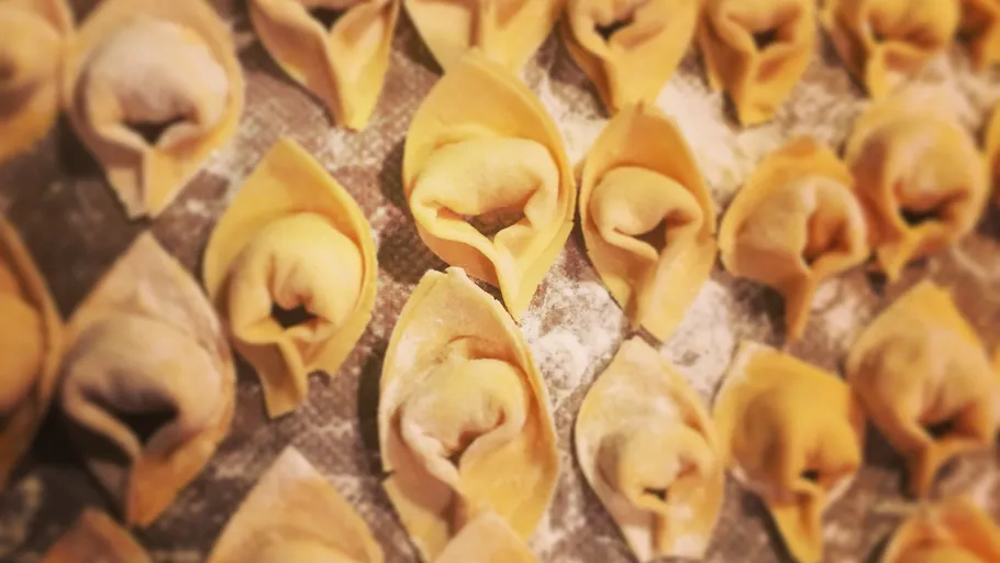 Close-up of uncooked tortellini on floured surface.