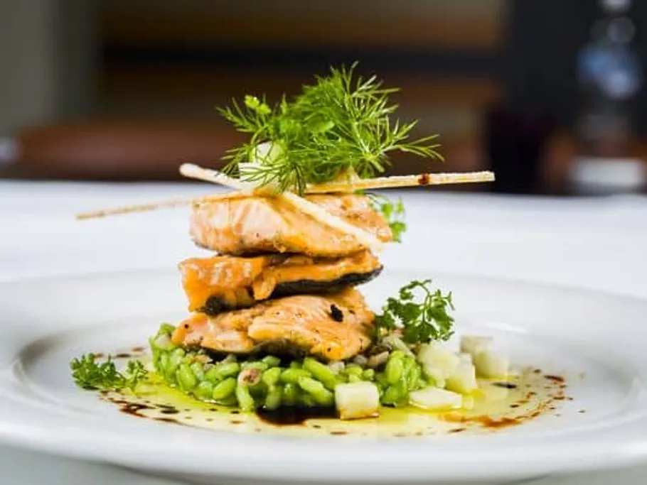 Salmon fillet on green risotto, garnished with herbs.
