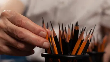 Hand greift Bleistift aus Behälter auf Tisch.