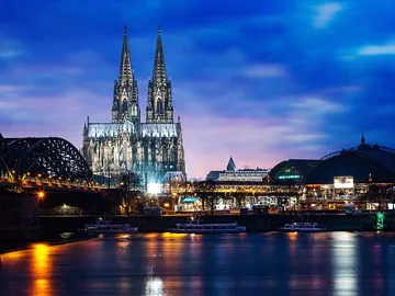 Kölner Dom erstrahlt nachts im Wasser mit Stadtlandschaft.