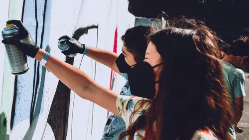 People spray painting mural on wall outside.
