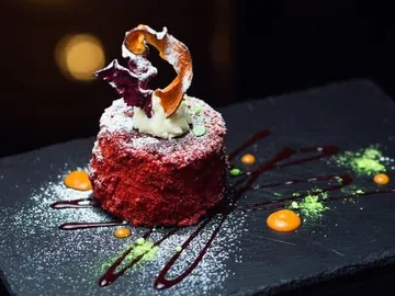 Red cake with cream, decoration and sauce on black plate.